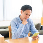 部屋でスマホを見る男性